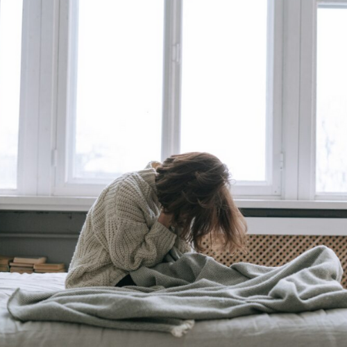 femme assise sur un lit épuisée avec la tête dans les mains